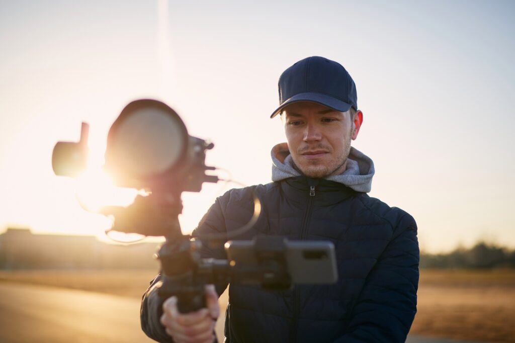 Young man filming with camera and gimbal. Portrait of videographer at beautiful sunrise.